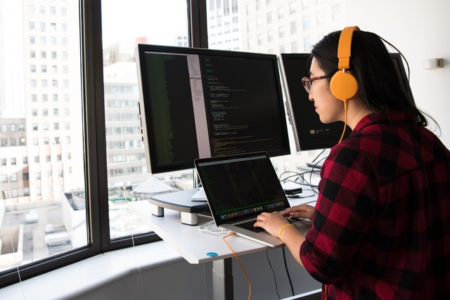 A female accessibility engineer wearing headphones using a laptop computer.